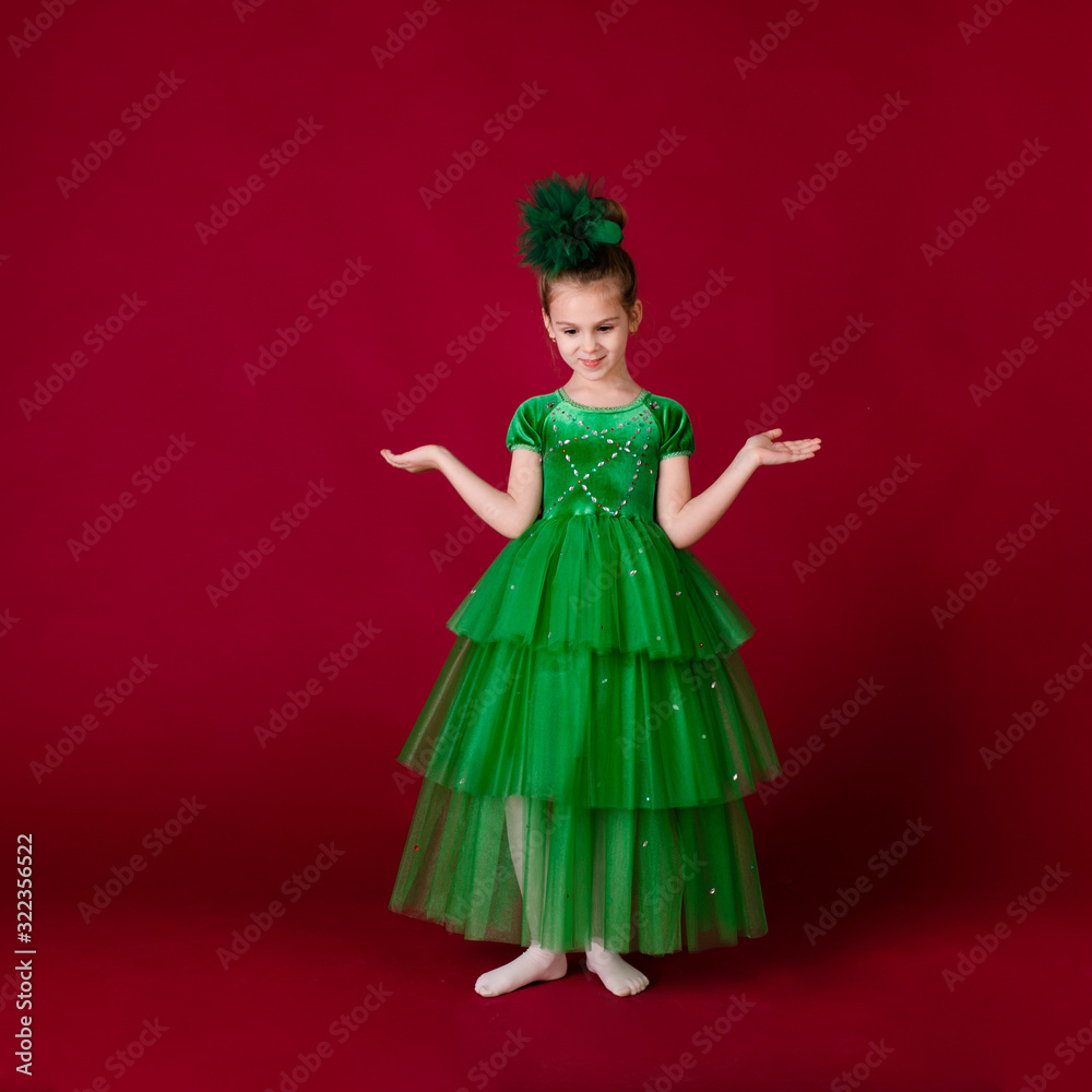 Beautiful little girl princess dancing in luxury green dress isolated on red background. Carnival party with costumes Beautiful little girl princess dancing in luxury green dress isolated on red background. Carnival party with costumes