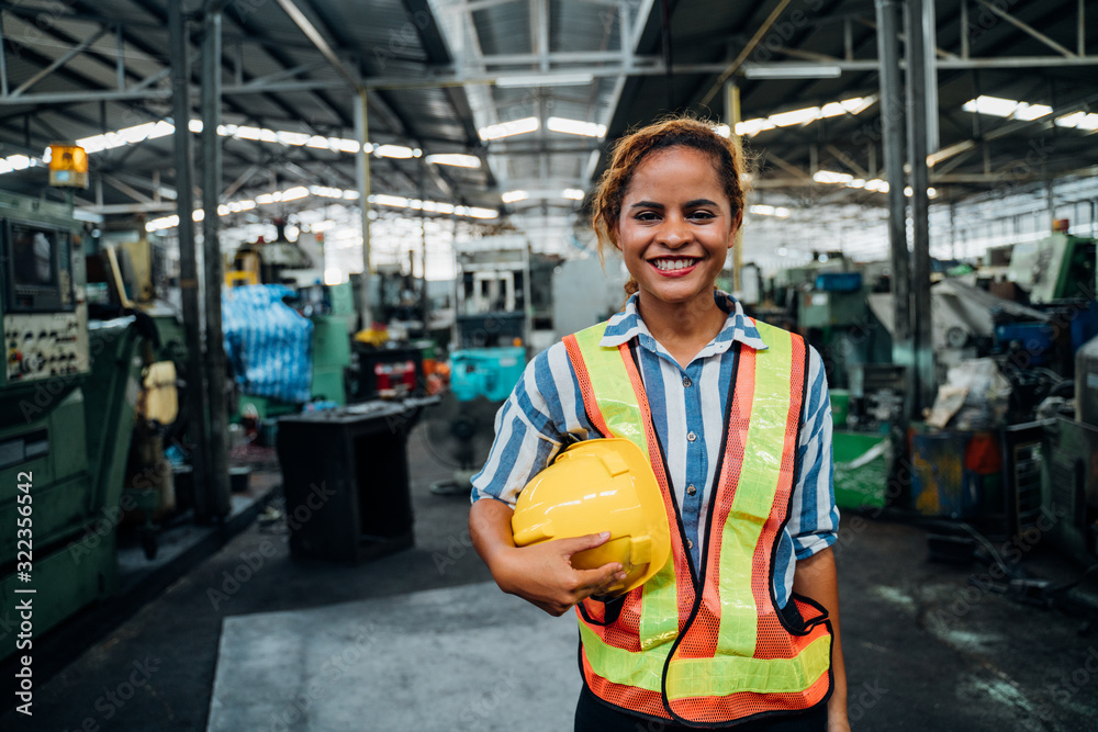attractive young african woman smiling and working engineering in industry.Portrait of young female worker in the factory.Work at the Heavy Industry Manufacturing Facility concept. - obrazy, fototapety, plakaty 
