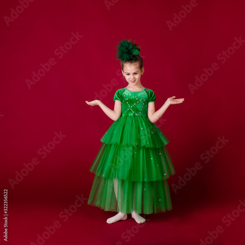 Beautiful little girl princess dancing in luxury green dress isolated on red background. Carnival party with costumes