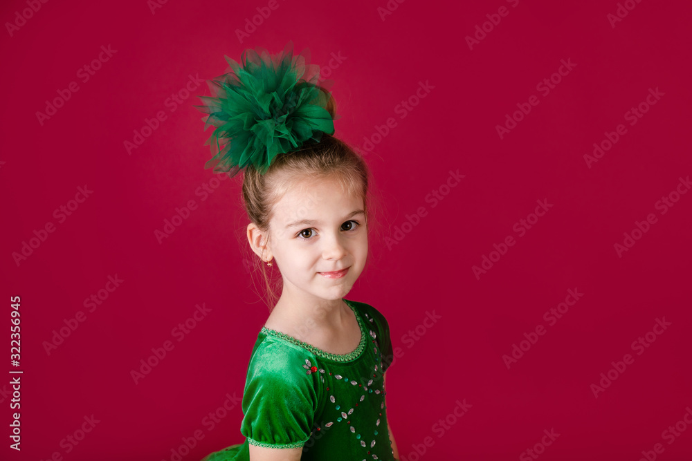 Beautiful little girl princess dancing in luxury green dress isolated on red background. Carnival party with costumes Beautiful little girl princess dancing in luxury green dress isolated on red background. Carnival party with costumes