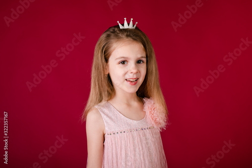 Beautiful little girl princess dancing in luxury pink and silver dress isolated on red background. Funny face, different emotions