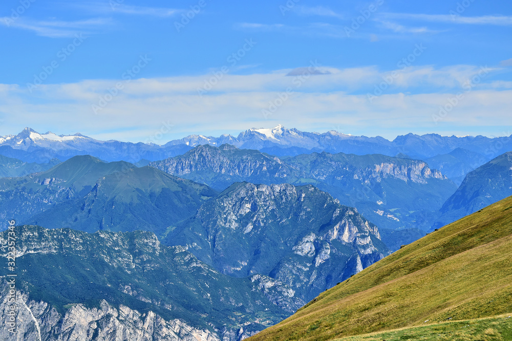 Malcesine, Italy - Monte Baldo, alpine mountains, yellow-green grass, blue sky with clouds, in the summer afternoon.