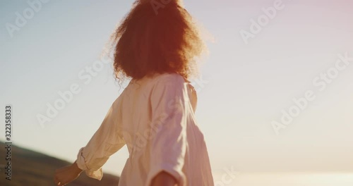 Young stylish carefree african american woman raising her arms joyfully at sunset embracing life to the fullest, happy smiling black woman expressing joy and contentment in her life photo