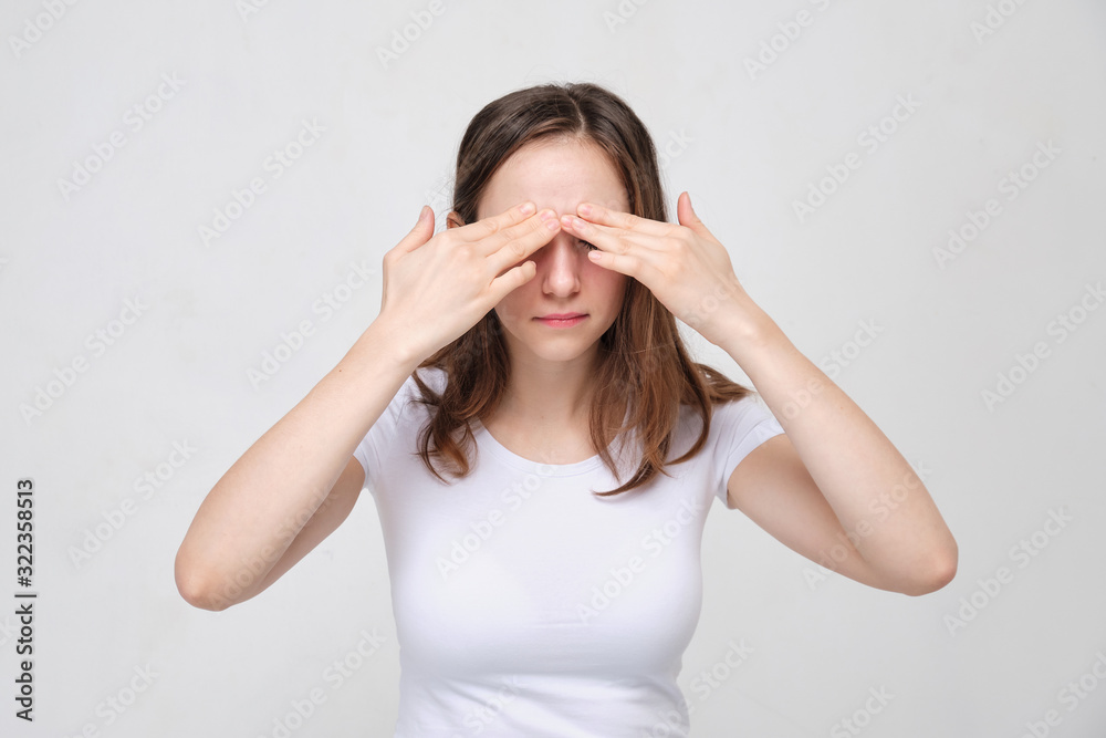 A girl in a white T-shirt massages her eyelids. The concept of severe pain in front of the head. A girl in a white T-shirt massages her eyelids. The concept of severe pain in front of the head.