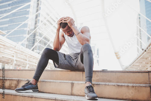 A 31 year old African American man with black skin he is and athlete, He is stressed and headache while he is sitting on the stairs at the train station, to people and health care concept.