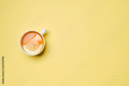 A cup of tea with lemon on a yellow paper background. Top view.