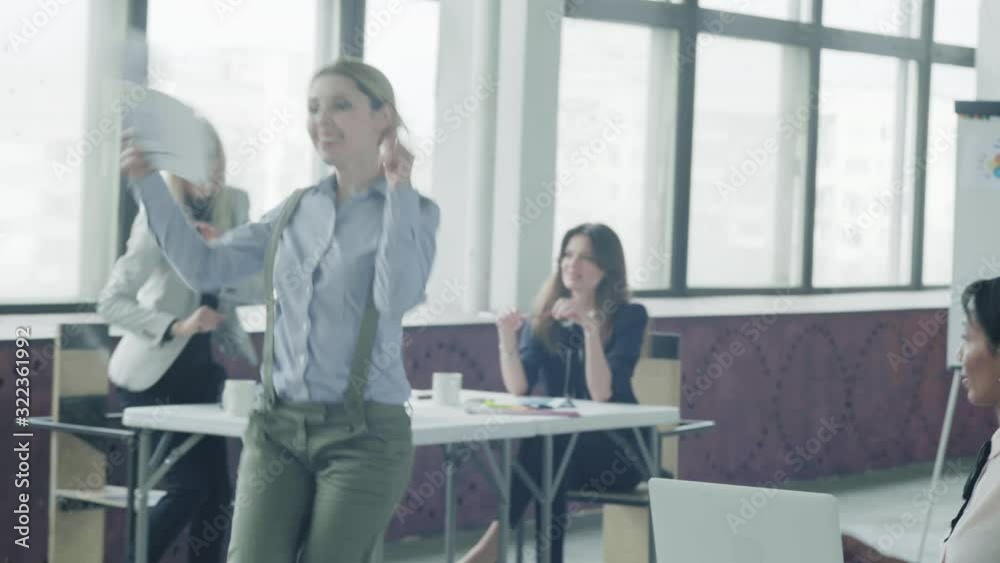 The girl manager is walking around the office, dancing and throwing documents. Together with her, colleagues begin to dance. Coworking. Office life. Hand camera