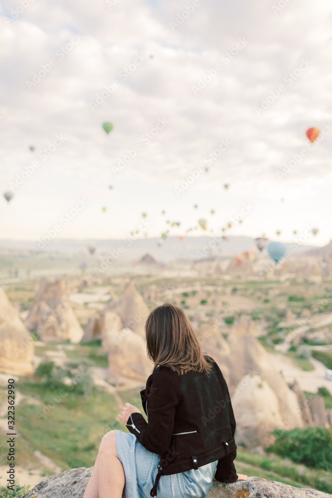 Woman watching colorful hot air balloons flying over the valley at Cappadocia, Turkey.Turkey Cappadocia fairytale scenery of mountains