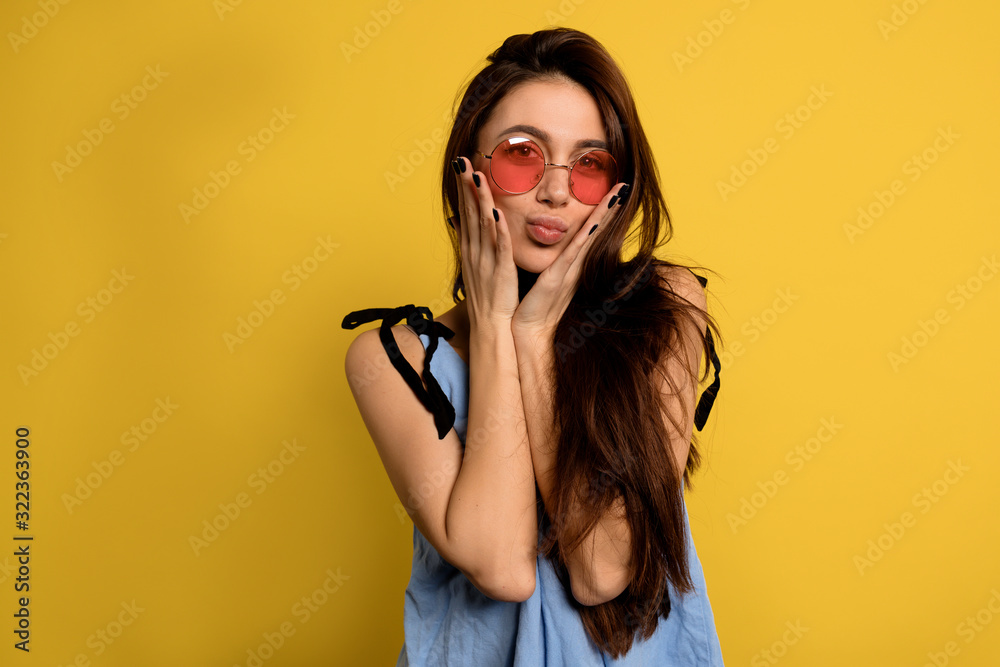 Inside close up portrait of charming funny girl in round pink glasses make a faces over yellow background