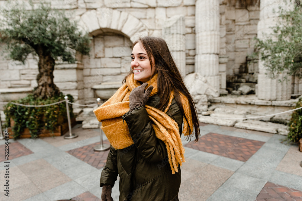 Happy beautiful girl having fun walking near castle. Young smiling woman in green jacket and yellow scarf travel around old wonderful European city. Lovely girl posing in the old street