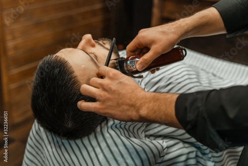 Beauty shop for men. Shaving a beard in a barbershop. Barber cuts his beard with a razor and clipper. close up Brutal haircuts. Hairdresser equipment. Selective focus.