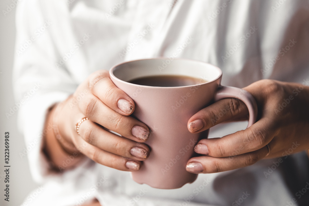 Woman in a white t-shirt holds morning coffee in a pink ceramic cup. Manicure. Front view
