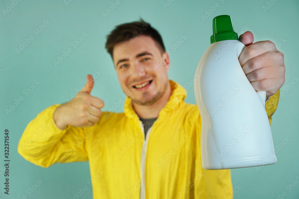 Happy Cleaner In A Yellow Suit Holds A Bottle Of Cleaning Product And Shows Thumb Up On A Blue Background Happy Cleaner In A Yellow Suit Holds A Bottle Of Cleaning Product And Shows Thumb Up On A Blue Background