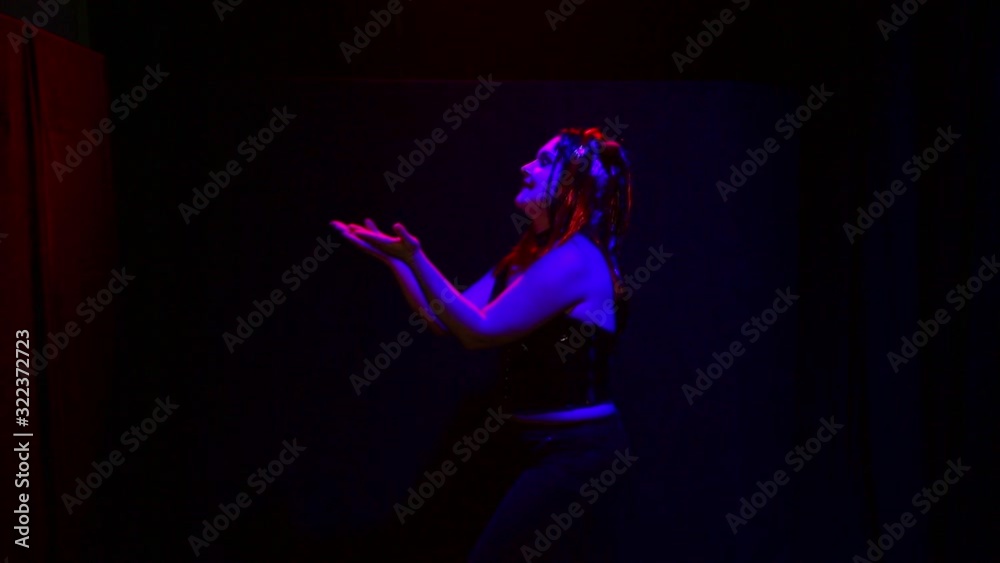 A woman in the form of a devil with an ominous smile dances in red lighting on a black background A woman in the form of a devil with an ominous smile dances in red lighting on a black background