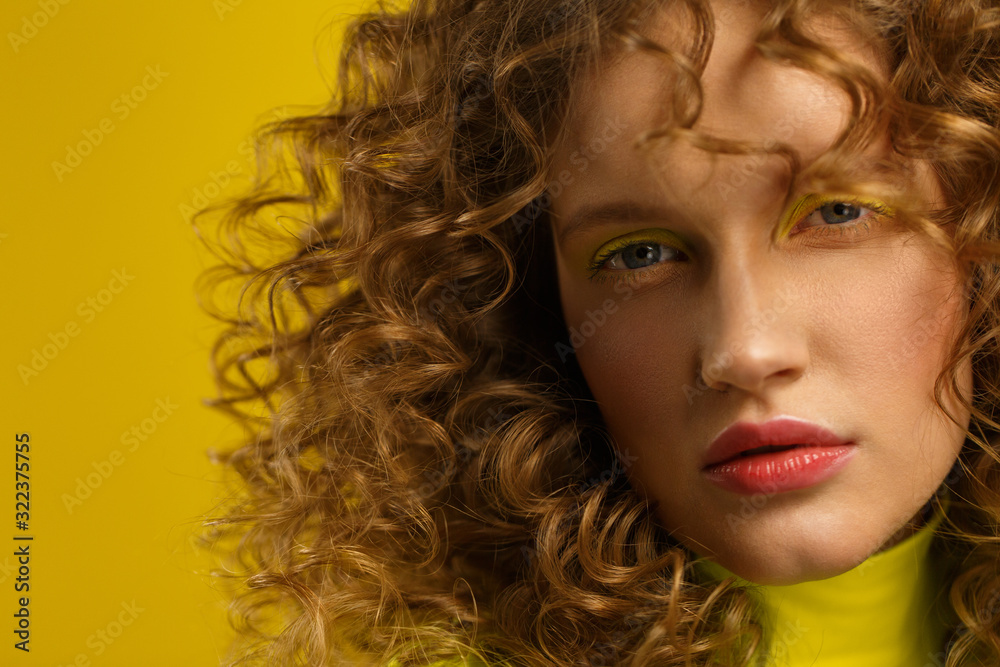 Close up fashion studio portrait of young beautiful women with curly hair.Nice girl with wavy hairstyle and bright make up isolated over yellow background.Beauty and hair care concept,yellow lifestyle