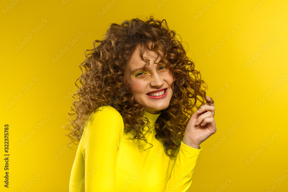 Portrait of young beautiful smiling women with curly hair. Happy girl with wavy hairstyle and bright make up isolated over yellow background. Beauty and hair care concept. Yellow lifestyle.Copy space. Portrait of young beautiful smiling women with curly hair. Happy girl with wavy hairstyle and bright make up isolated over yellow background. Beauty and hair care concept. Yellow lifestyle.Copy space.