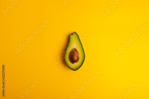 Ripe juicy halved  avocado on a yellow solid background with copy space. Vegan, vegetarian, raw organic food template. Eco detox style.