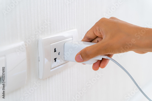 Woman's Hand Inserting Electrical Power Cord Plug into Receptacle on wall outlet.
