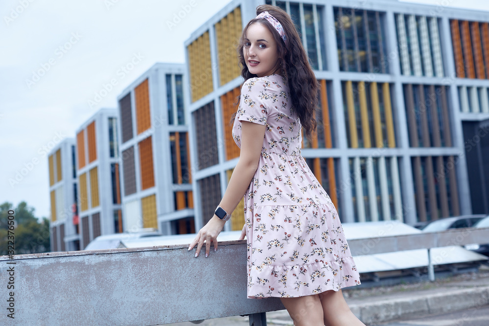 Young beautiful bright girl in a summer dress standing on a bridge