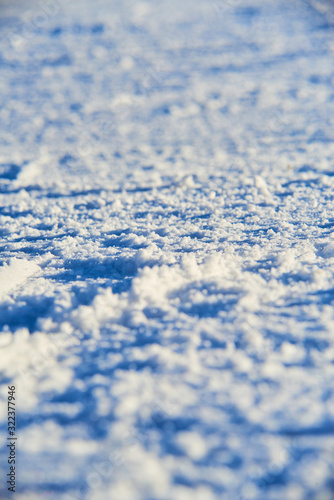 Groomed snowy ski slope with trace from skis and snowboards at sun winter day. Low depth of field. Selective focus