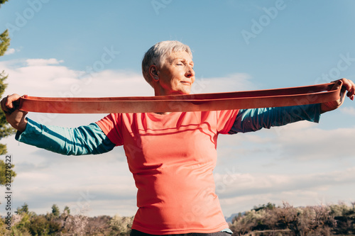 older woman with red t-shirt and elastic band practicing sport in the field photo