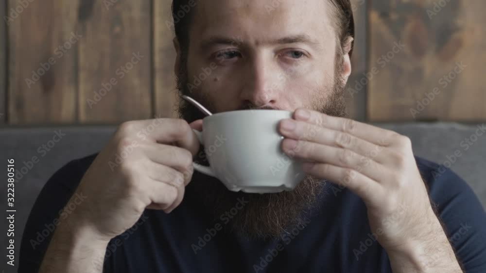 Close up shot of a bearded man drinking cappuccino indoor cozy city cafe wood planks wall background natural light Close up shot of a bearded man drinking cappuccino indoor cozy city cafe wood planks wall background natural light