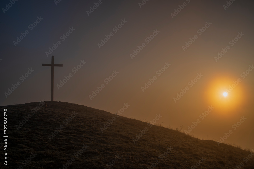 Sunrise on Radobyl hill with big cross and small statue in winter morning