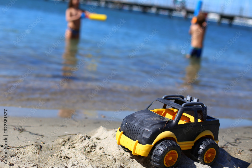 Children toy car jeep of black and yellow color on sand near the water on the beach of blue sea. Boys play water guns. Vacation with kids on coast on warm sunny summer day. Tourism in Europe,Slovenia Children toy car jeep of black and yellow color on sand near the water on the beach of blue sea. Boys play water guns. Vacation with kids on coast on warm sunny summer day. Tourism in Europe,Slovenia