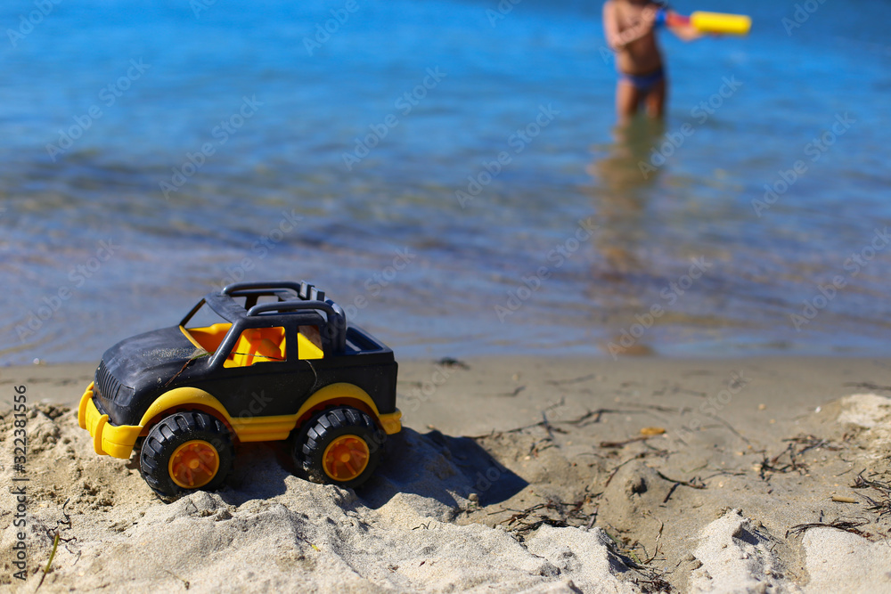 Children toy car jeep of black and yellow color on sand near the water on the beach of blue sea. Boys play water guns. Vacation with kids on coast on warm sunny summer day. Tourism in Europe,Slovenia Children toy car jeep of black and yellow color on sand near the water on the beach of blue sea. Boys play water guns. Vacation with kids on coast on warm sunny summer day. Tourism in Europe,Slovenia