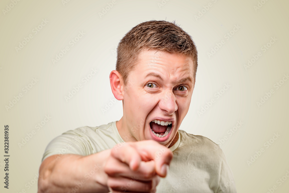 Young man shouts and pointing finger on a yellow background.