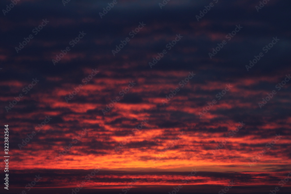 Crimson sky with clouds illuminated by the sun at sunset or sunrise at dusk