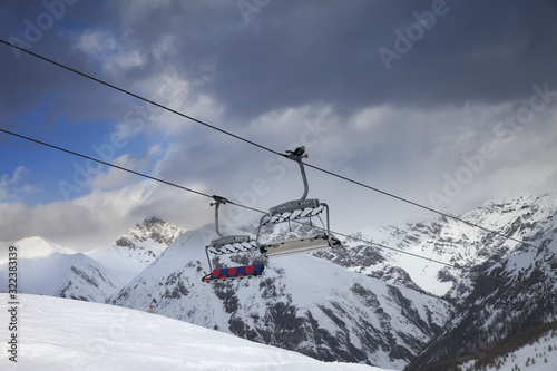 Sunlit chair lift, snowy ski slope, high winter mountains and dark cloudy sky