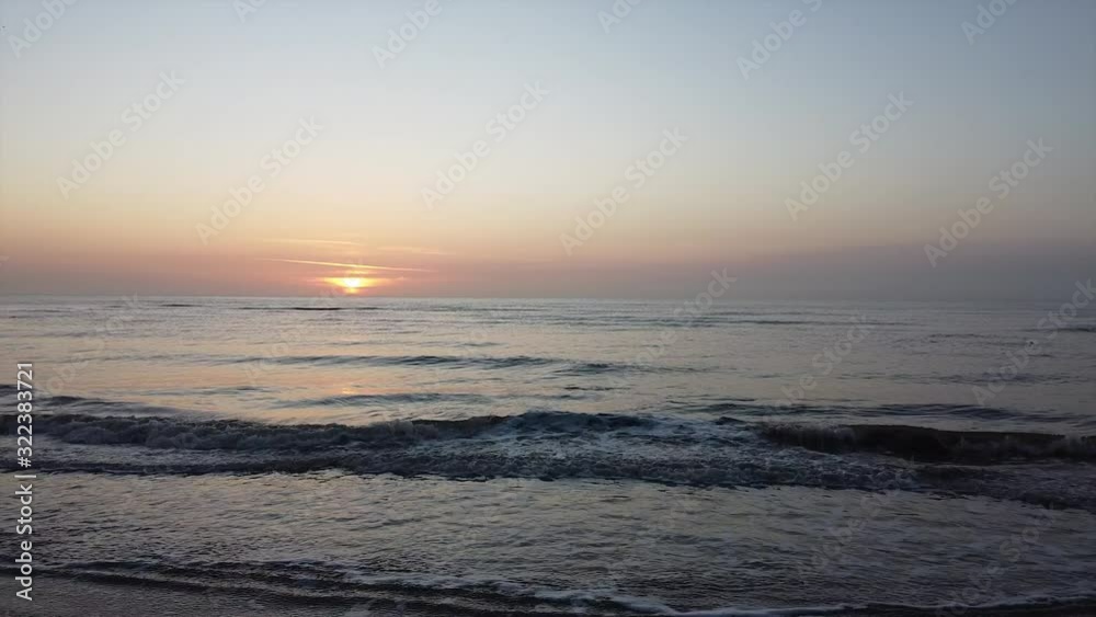 Drone dolly shot heading towards the sunset over the beach, calm ocean waves crashing on the sandy shore. Filmed in the winter but could almost be mistaken for a beautiful summer sunset at dusk. Drone dolly shot heading towards the sunset over the beach, calm ocean waves crashing on the sandy shore. Filmed in the winter but could almost be mistaken for a beautiful summer sunset at dusk.