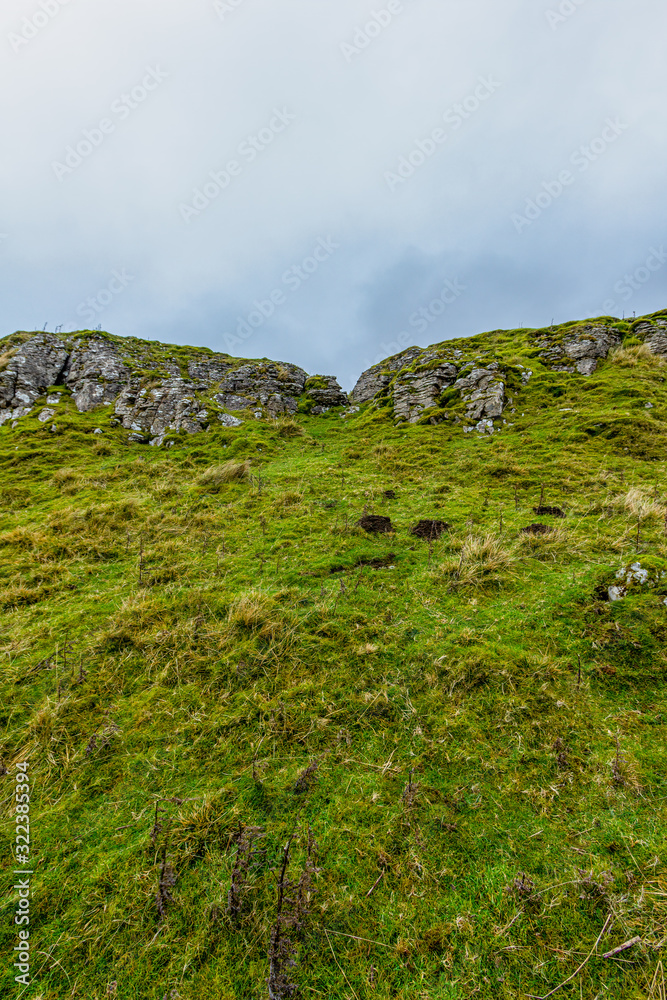 A scenic view of a mountain rock formation with grassy slope under a grey sky