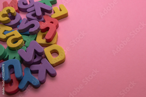 Colorful plastic alphabet letters on pink background with copy space, top view