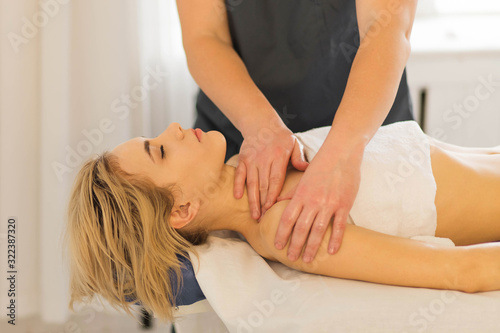 Hands of masseur making therapeutic neck massage for woman lying on couch in beauty spa salon. Body correction, treatments and relaxing. Close up
