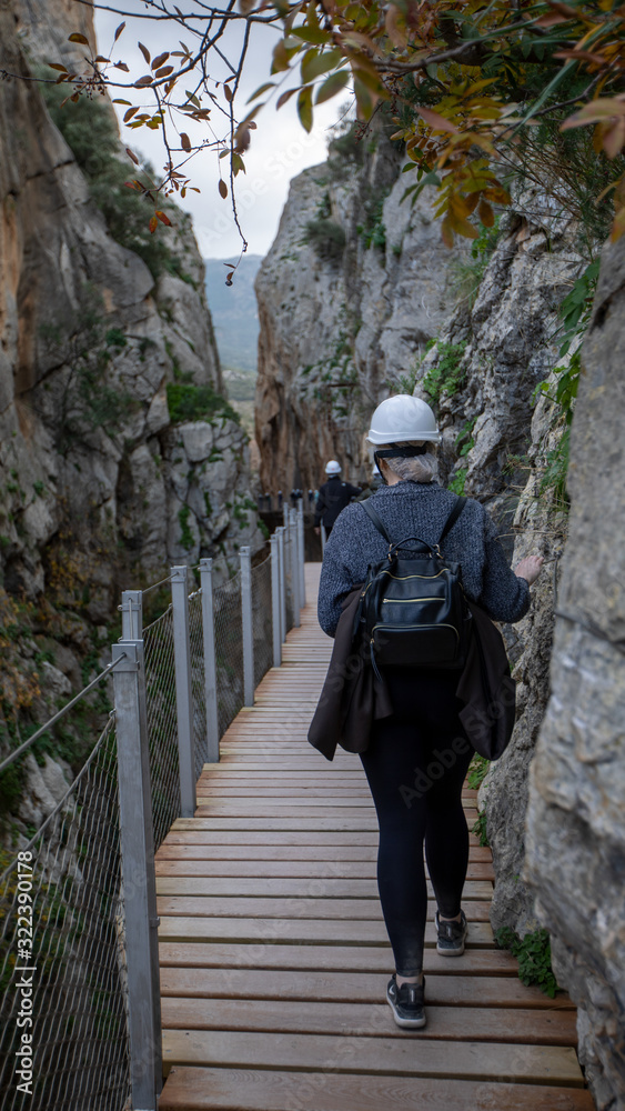 Woman crossing a narrow pass through rocks hills and wearing a white helmet.