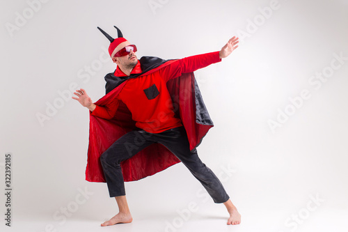 Stylish elegant man in black red halooween costume and devil horns posing like an eccentric actor over white studio background. photo