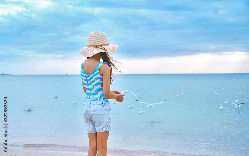 Little cute girl in hat feeds seagulls on the beach.