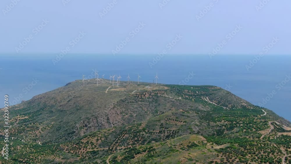 Drone view above mountain approaching wind turbines in distance, blue ocean water background unobstructed view