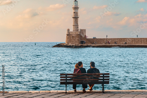 young couple in love sitting on a bench by the sea on the waterfront of the Greek city of Chania. © westermak15