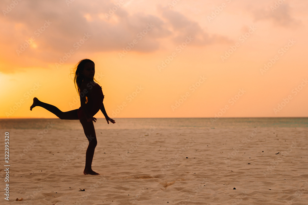 Adorable happy little girl on white beach at sunset.