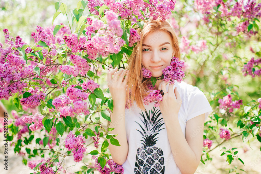 Handsome woman with red hair and pretty smile posing in lilac garden with flowers and enjoys the smell Handsome woman with red hair and pretty smile posing in lilac garden with flowers and enjoys the smell