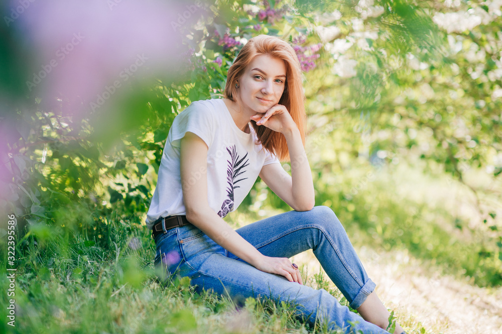 Portrait of emotional red-hair girl sits in a lilac garden Portrait of emotional red-hair girl sits in a lilac garden
