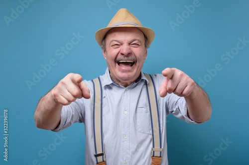 Joyful senior hispanic man pointing at you laughing. Funny joke or prank concept. photo