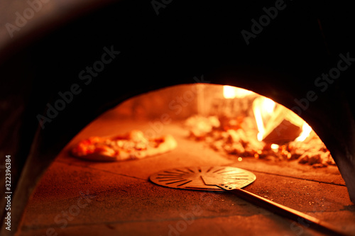 Baked tasty margherita pizza in Traditional wood oven in Naples restaurant, Italy. Original neapolitan pizza. Red hot coal. © malkovkosta