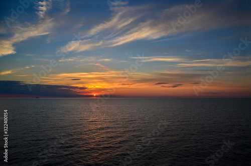 Sun is setting behind the Baltic Sea. The sky is colorful combination of yellows, oranges and blues. The photo is a dramatic because of the big clouds, and sea with waves. Very scenic.