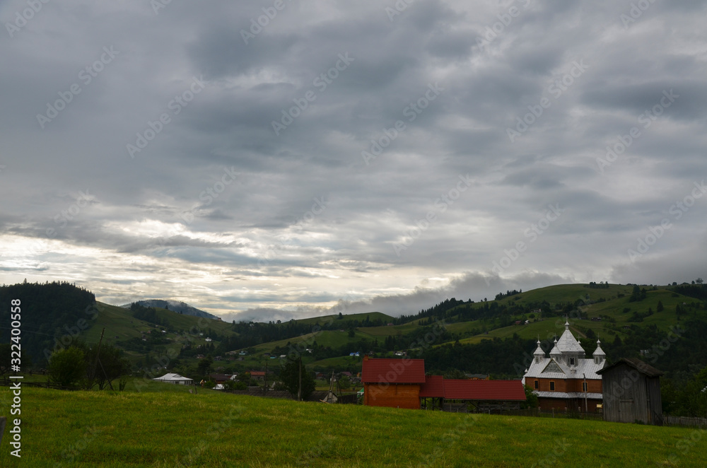 Obraz premium Modest houses of the Carpathian village in the valleys near the green mountains . For your design