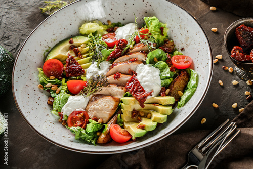 Healthy salad with fillet chicken, avocado, tomatoes, lettuce, greens, pine nuts and sauce in bowl on wooden background. Healthy food, clean eating, dieting, Buddha bowl, close up