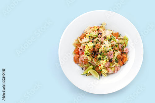 Healthy fresh salad with lettuce, greens, red caviar, shrimp, fillet salmon in plate isolated on blue background. Healthy food, clean eating, dieting, top view